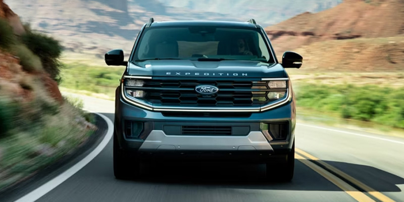 Green Ford Expedition SUV driving on a winding road through a mountainous landscape.